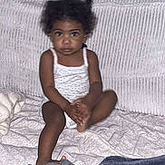 Shaïly participe au concours pour gagner de l'argent avec cette photo : toddler, child, sitting, couch, blanket, indoors, curly_hair, looking_at_camera, casual_clothing, patterned_fabric, face, young_child, home, relaxed, barefoot, small_person, infant, portrait, soft_lighting, cozy