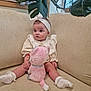 baby, child, infant, stuffed_animal, plush_toy, couch, sofa, headband, socks, plant, leaves, indoor, cute, seated, clothing, soft_toy, home, portrait, young_child, furniture