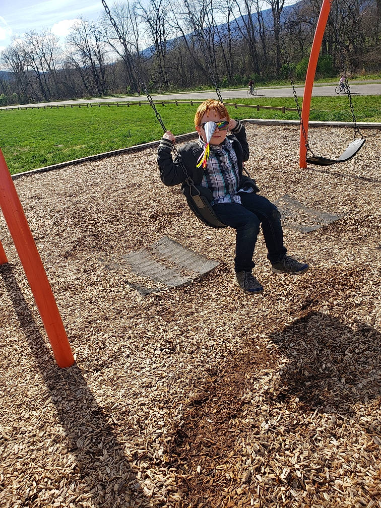 Antonio is registered to the contest to win money with this photo: city, fun, grass, human_settlement, outdoor_play_equipment, park, person, plant, play, playground, public_space, recreation, soil, swing, tree