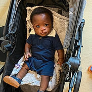 Ty'Aire Avant joined the competition — help win amazing prizes! baby, child, stroller, navy_blue_outfit, blue_shoes, blanket, indoor, floor, curious, portrait, person, cute, infant, footwear, seated, black_hair, looking_at_camera, soft_texture, casual_clothing, orange_sandals