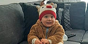 Thibaut participe au concours pour gagner de l'argent avec cette photo : baby, child, clothing, couch, cozy, curtains, cute, furniture, home, indoor, living_room, pillow, reindeer_hat, relaxed, sitting, smiling, soft_toys, toddler, warm_clothes, window