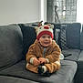 baby, child, clothing, couch, cozy, curtains, cute, furniture, home, indoor, living_room, pillow, reindeer_hat, relaxed, sitting, smiling, soft_toys, toddler, warm_clothes, window