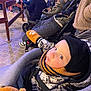 baby, blue_eyes, bundle, child, crowd, curious, face, hat, jacket, mittens, outdoor, pavement, people, portrait, scarf, seated, stroller, toddler, warm_clothing, winter_clothing