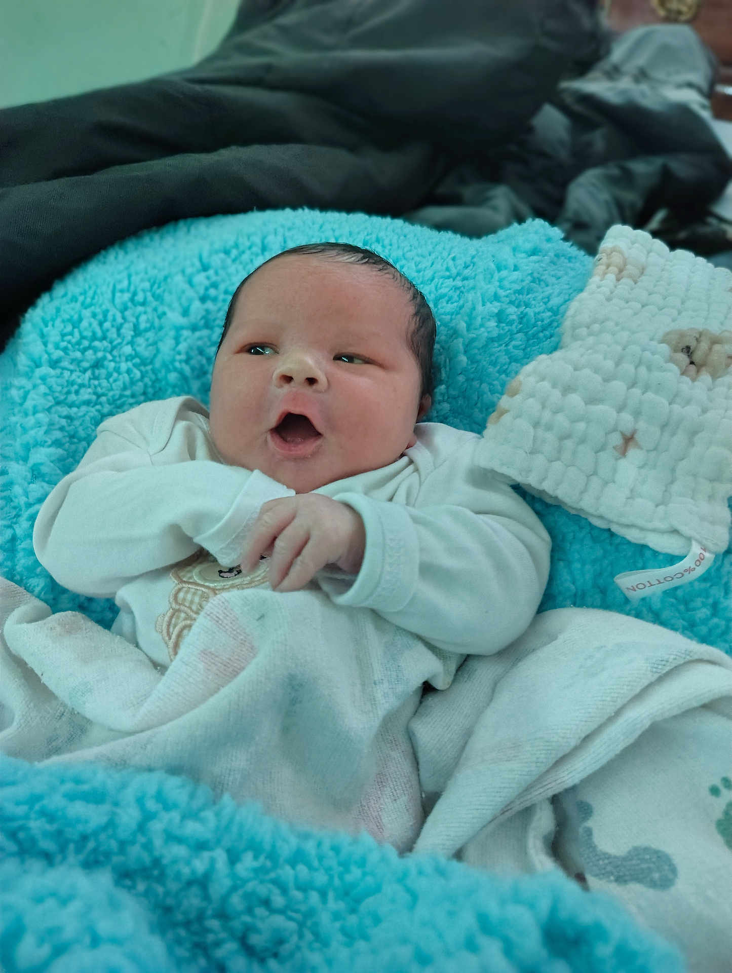 Layton is registered to the contest to win money with this photo: baby, newborn, infant, blanket, blue_blanket, plush, swaddle, clothing, face, eyes, mouth, hands, cozy, portrait, soft_texture, bed, towel, cute, sleepy, skin