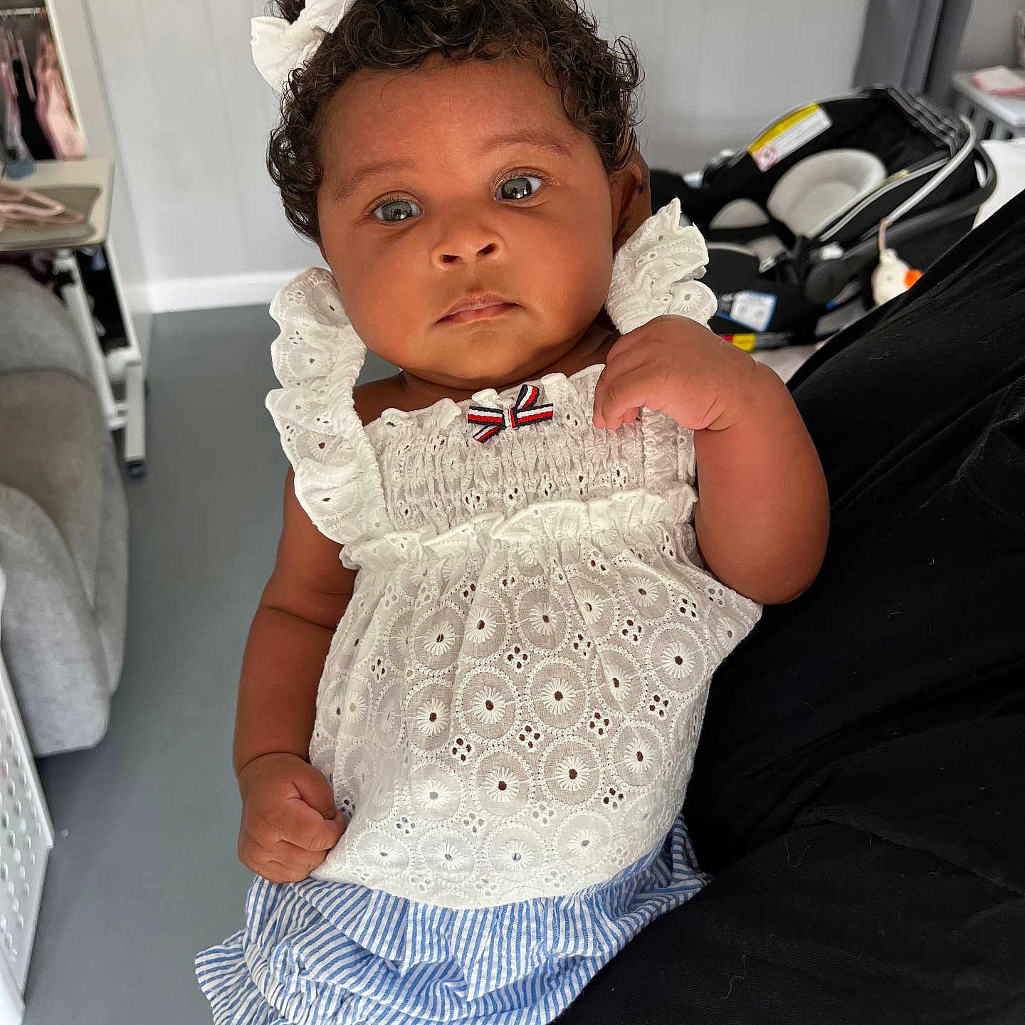 Charlotte Elizabeth is registered to the contest to win money with this photo: baby, car_seat, child, clothing, curly_hair, cute, expression, face, floor, hand, holding, home, indoor, infant, person, portrait, striped_shorts, white_bow, white_top, young_child