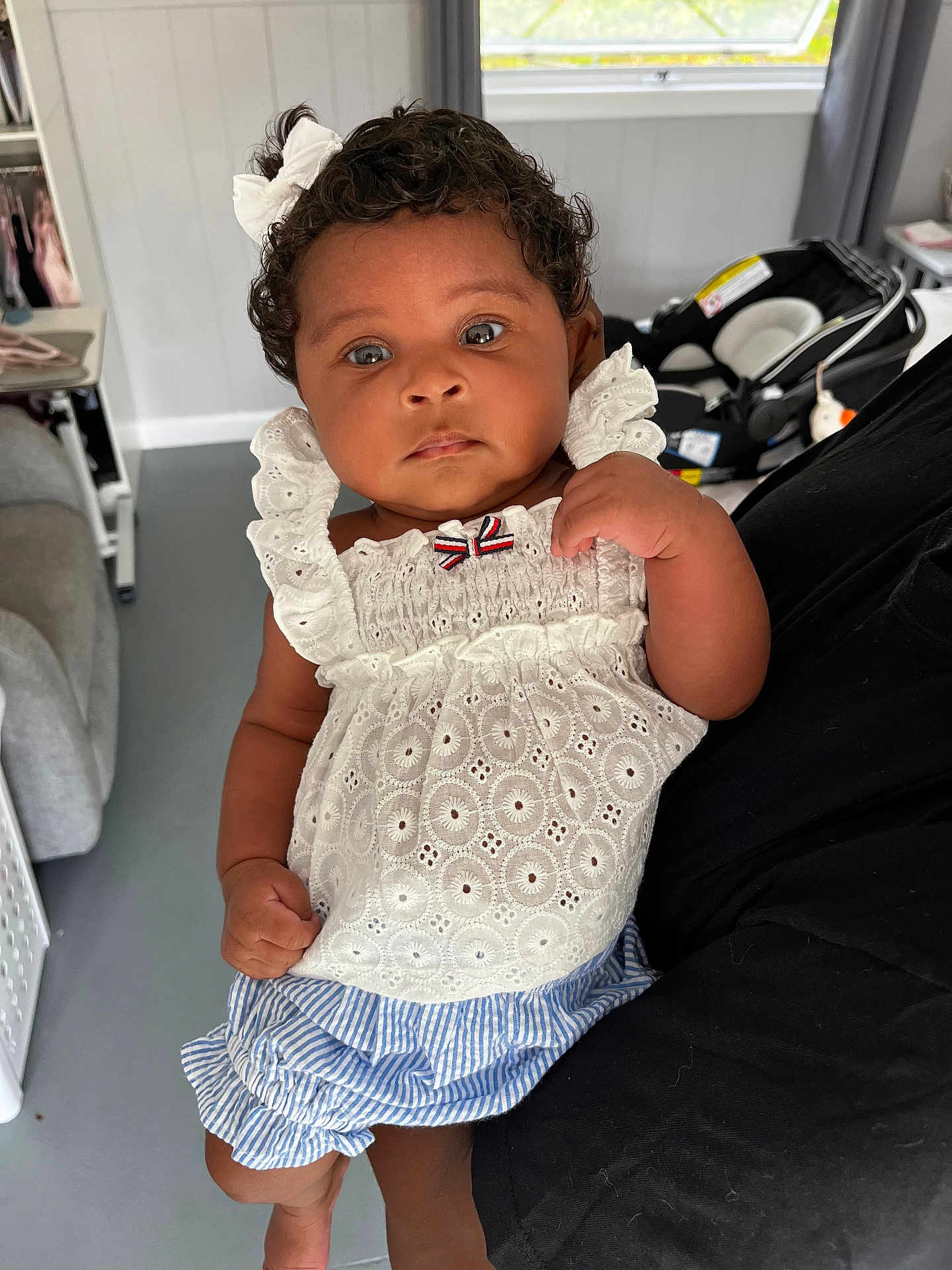 Charlotte Elizabeth is registered to the contest to win money with this photo: baby, child, curly_hair, white_bow, white_top, striped_shorts, indoor, person, car_seat, holding, cute, portrait, infant, clothing, hand, face, expression, young_child, home, floor