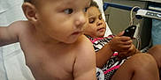 Xander joined the competition — help win amazing prizes! baby, child, hospital, medical_equipment, bed, remote_control, cabinet, indoors, person, healthcare, toddler, patient, furniture, curly_hair, skin, clothing, young_child, sitting, looking_away, room