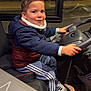 Andrea participe au concours pour gagner de l'argent avec cette photo : child, smile, steering_wheel, vehicle_interior, seat, jacket, sneakers, tracksuit, hands_on_wheel, reflection, window, night, portrait, candid, happy, driver_imitation, seatbelt_booster, adult_reflection, indoors, transport