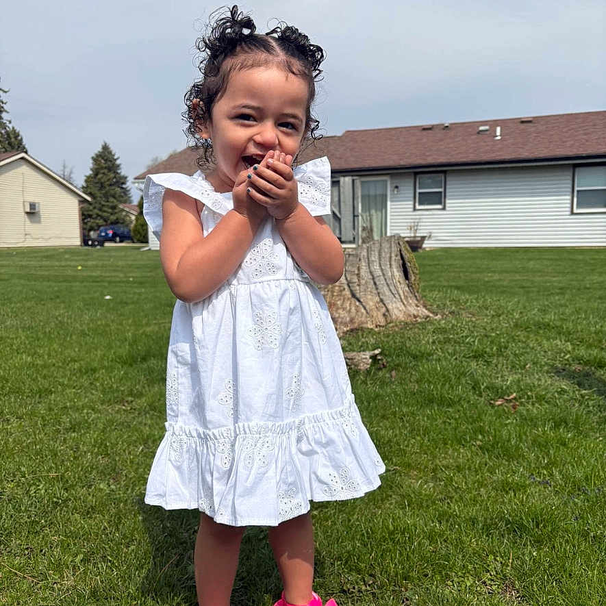 Jayliyah is registered to the contest to win money with this photo: child, curly_hair, cute, daylight, footwear, girl, grass, hair_buns, happy, house, lawn, nature, outdoor, person, pink_sandals, playful, residential, smiling, summer, white_dress