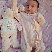 Skylar is registered to the contest to win money with this photo: baby, infant, pink_onesie, plush_toy, bunny, blanket, soft_texture, cute, lying_down, young_child, face, person, child, indoor, comfort, sleepwear, toy, pink, newborn, cozy