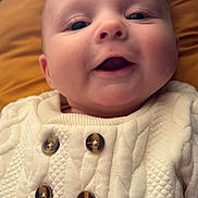 Gianni participe au concours pour gagner de l'argent avec cette photo : baby, infant, face, smile, close_up, portrait, sweater, buttoned_sweater, quilted_texture, cozy, blanket, bedding, lying_down, cheeks, eyes, nose, mouth, cute, indoor, warm_colors