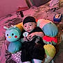 baby, infant, black_clothing, cap, plush_pillow, caterpillar_pillow, blanket, toy, socks, pacifier_clip, floor, indoor, child, cozy, soft_lighting, cute, relaxed, person, home, carpet