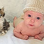 baby, kitten, cat, infant, knitted_hat, cute, animal, pet, child, tummy_time, white_blanket, soft, curious, indoors, playmat, colorful, furry, small, young, portrait