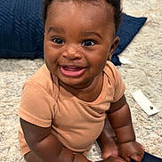 Prince is registered to the contest to win money with this photo: baby, smiling, infant, sitting, onesie, carpet, blue_pillow, happy, cute, child, indoor, portrait, skin, face, eyes, hands, feet, clothing, young, person