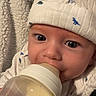 baby, bottle, feeding, hat, dinosaur_pattern, onesie, blanket, closeup, face, infant, cute, child, indoors, soft_texture, cozy, portrait, big_eyes, sleepwear, warm, comfort