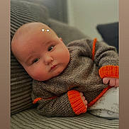 George is registered to the contest to win money with this photo: baby, infant, child, sweater, orange_cuffs, couch, ribbed_fabric, indoor, portrait, cute, chubby_cheeks, cozy, knitwear, relaxed, pout, face, human, person, warm_clothing, soft_lighting