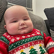 George joined the competition — help win amazing prizes! baby, child, christmas_sweater, comfort, couch, cozy, face, furniture, green_sweater, head, holiday, indoor, knitwear, pattern, person, portrait, red_sweater, seated, smiling, window_blinds