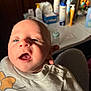 Lyam a rejoint le concours — aidez-le/la à gagner de superbes lots ! baby, infant, face, eyes, mouth, clothing, shirt, person, hand, indoor, blurred_background, table, bottle, skin, head, expression, newborn, holding, closeup, light