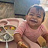 Aitana is registered to the contest to win money with this photo: baby, child, infant, smiling, happy, eating, food, high_chair, pink_clothing, messy_face, portrait, indoor, living_room, sofa, window, sunlight, table, plate, spoon, home