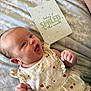 Esme joined the competition — help win amazing prizes! baby, smiling, infant, dress, bed, blanket, card, pattern, happy, cute, child, person, lying_down, face, hand, skin, fabric, text, closeup, expression
