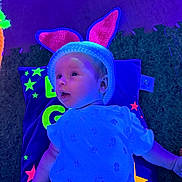 Esme is registered to the contest to win money with this photo: baby, child, bunny_ears, hat, pillow, stars, colorful, blue_light, purple_light, cute, infant, laying_down, knitted, clothing, soft_texture, indoor, portrait, curious, small_hand, toddler