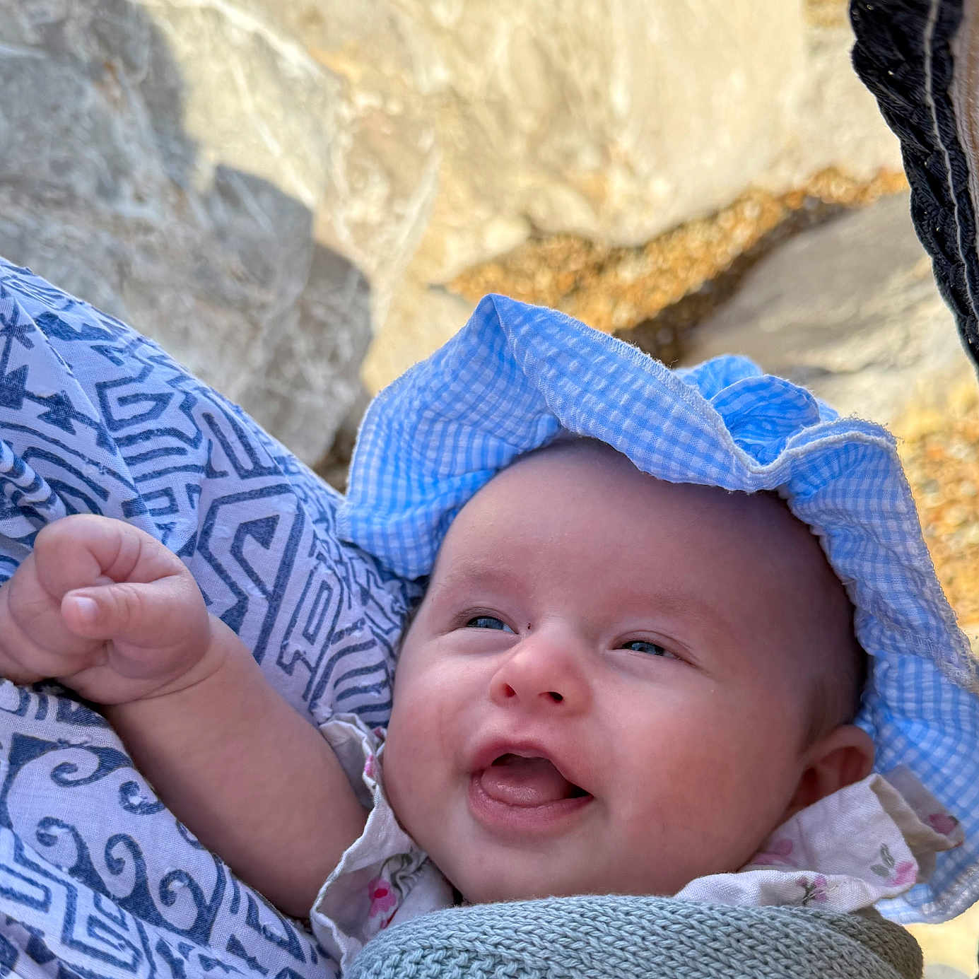 Esme joined the competition — help win amazing prizes! baby, blanket, blue_hat, cheeks, close_up, cute, expression, hand, happy, hat, headwear, infant, knitted_blanket, nature, outdoor, person, rock, skin, smiling, sunlight