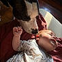 baby, dog, sleeping, onesie, dinosaur_pattern, blanket, indoor, natural_light, pet, child, animal, cozy, peaceful, cute, infant, mammal, face, resting, closeup, tender_moment