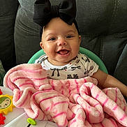 Ariella is registered to the contest to win money with this photo: baby, black_bow, blanket, pink_blanket, smiling, happy, infant, toy, chair, headband, cute, child, indoors, cozy, clothing, face, person, seated, plaything, soft