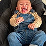 baby, smiling, denim_overalls, beige_shirt, black_cushion, infant, happy, sitting, feet, hands, cute, child, portrait, indoors, clothing, face, joyful, comfortable, candid, young