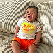 Nahyl participe au concours pour gagner de l'argent avec cette photo : baby, child, smiling, sitting, couch, clothing, nike, orange_shorts, white_tshirt, happy, indoors, person, face, shorts, apparel, infant, home, cute, leisure, comfortable
