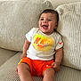 baby, child, smiling, sitting, couch, clothing, nike, orange_shorts, white_tshirt, happy, indoors, person, face, shorts, apparel, infant, home, cute, leisure, comfortable