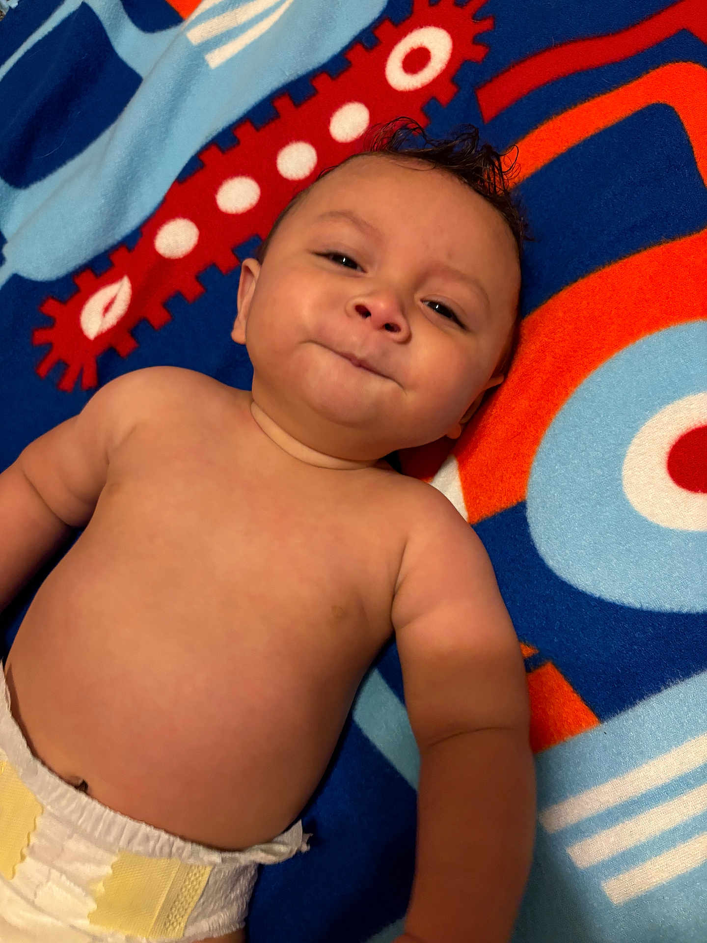 Mateo is registered to the contest to win money with this photo: baby, infant, diaper, smile, face, skin, arm, blanket, pattern, colorful, cute, child, lying_down, expression, indoors, human, young, playful, portrait, soft