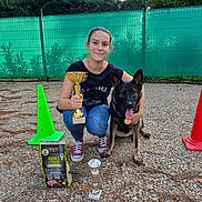 Mya participe au concours pour gagner de l'argent avec cette photo : woman, person, dog, german_shepherd, pet, animal, outdoor, sports, competition, trophy, championship, dog_training, training_cone, dog_food, fence, gravel, garden, portrait, sitting, award