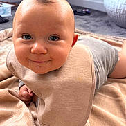 Teddie is registered to the contest to win money with this photo: baby, bib, blanket, smile, face, child, indoor, clothing, onesie, drool, head, skin, person, cute, infant, happy, young_child, carpet, room, portrait