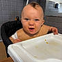 Teddie is registered to the contest to win money with this photo: baby, highchair, food, messy, kitchen, child, face, expression, mouth_open, blue_eyes, mohawk, bib, tray, table, indoor, person, skin, hand, clothing, seat