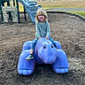 Octavia is registered to the contest to win money with this photo: child, playground, slide, blue_turtle, sculpture, smiling, curly_hair, outdoor, park, play_equipment, grass, woodchips, casual_clothing, daytime, happy, toy, recreation, nature, leisure, person