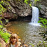 child, waterfall, nature, rocks, greenery, smiling, peace_sign, outdoor, water, river, trees, leaves, happy, portrait, sunlight, forest, person, daylight, playful, scenery