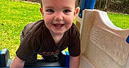 Isaiah is registered to the contest to win money with this photo: toddler, child, smiling, playground, outdoor, grass, plastic, play_structure, happy, young_child, climbing, blue, green, nature, person, toy, casual_clothing, daylight, fun, cute