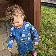 Isaiah joined the competition — help win amazing prizes! toddler, child, curly_hair, blue_sweater, space_pattern, jeans, sneakers, grass, outdoor, wooden_post, paving_stones, happy, smiling, walking, playground, daylight, casual_clothing, person, cute, nature
