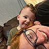 Isaiah is registered to the contest to win money with this photo: toddler, adult, glasses, red_hair, smile, couch, leather, indoor, child, person, affection, happy, casual, closeup, portrait, face, head, playful, cozy, family