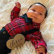 Kairann is registered to the contest to win money with this photo: baby, infant, three_months, plaid_shirt, bow_tie, suspenders, wooden_sign, heart_shaped_sign, blanket, soft_texture, cute, portrait, smiling, face, hand, clothing, lying_down, indoor, young_child, happy