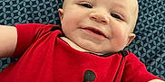 Ryder is registered to the contest to win money with this photo: baby, child, smiling, red_shirt, black_graphic, blue_blanket, patterned_blanket, portrait, face, head, skin, infant, person, cute, happy, indoors, laying_down, short_hair, mohawk, toddler