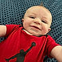 baby, child, smiling, red_shirt, black_graphic, blue_blanket, patterned_blanket, portrait, face, head, skin, infant, person, cute, happy, indoors, laying_down, short_hair, mohawk, toddler