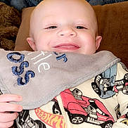 Ryder is registered to the contest to win money with this photo: baby, smiling, face, bib, clothing, onesie, car_pattern, hand, blanket, cushion, indoors, cozy, happy, child, infant, portrait, cute, warm, soft, sleepwear