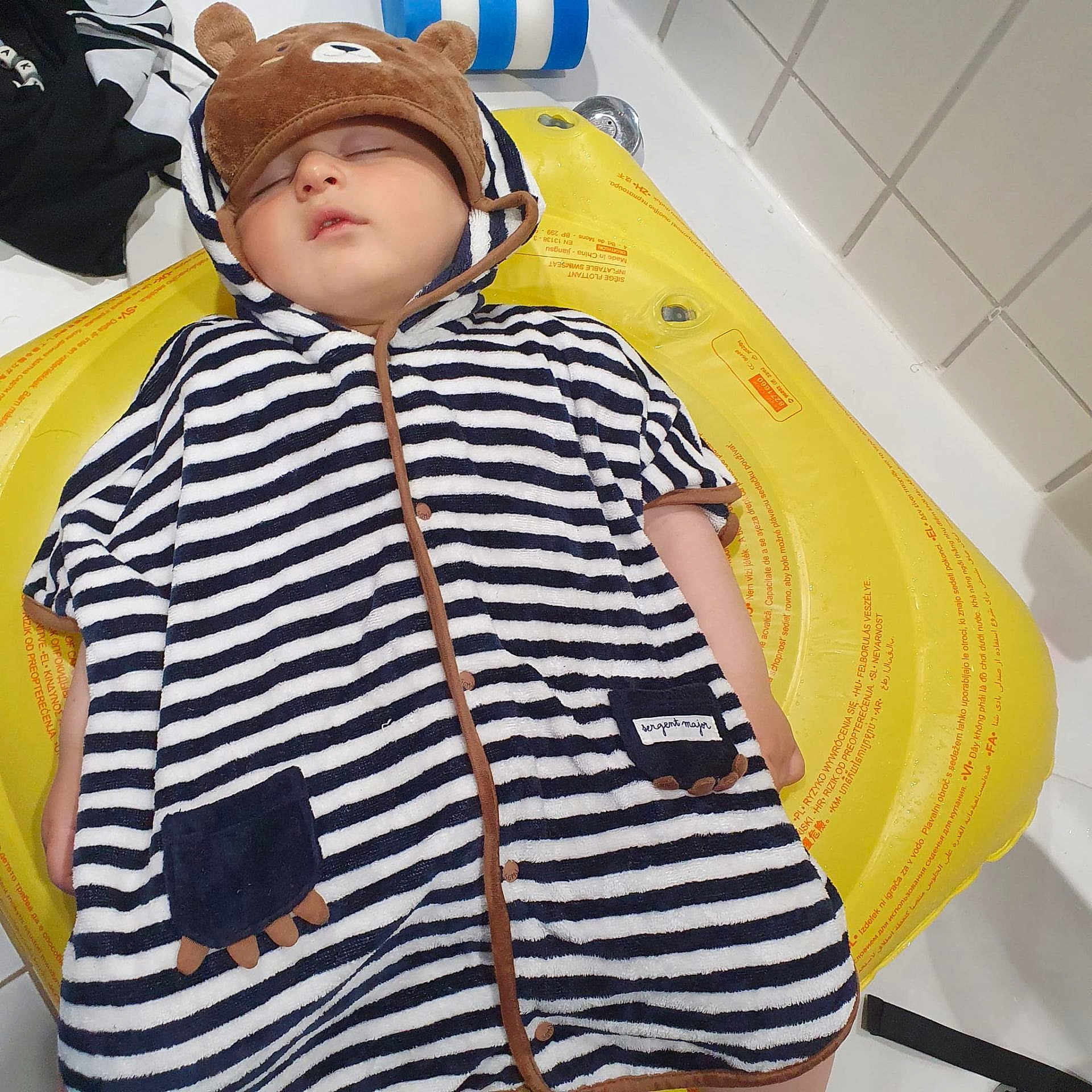 Sisil participe au concours pour gagner de l'argent avec cette photo : baby, sleeping, bear_hat, striped_clothing, hooded_outfit, yellow_inflatable, bathroom, tiled_wall, child, cute, peaceful, resting, infant, soft_fabric, pajamas, adorable, indoor, portrait, young_child, cozy