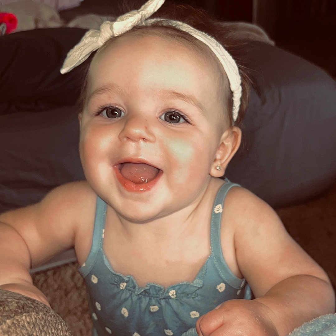 Kesley joined the competition — help win amazing prizes! baby, blanket, blue_dress, child, cozy, cute, expression, face, furniture, hand, happy, headband, indoor, infant, person, skin, smiling, soft, warm_lighting, young