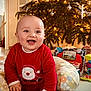 baby, child, smiling, christmas_tree, holiday, festive, indoors, red_clothing, toy, cushion, floor, decorations, lights, happy, sitting, cute, face, home, seasonal, celebration