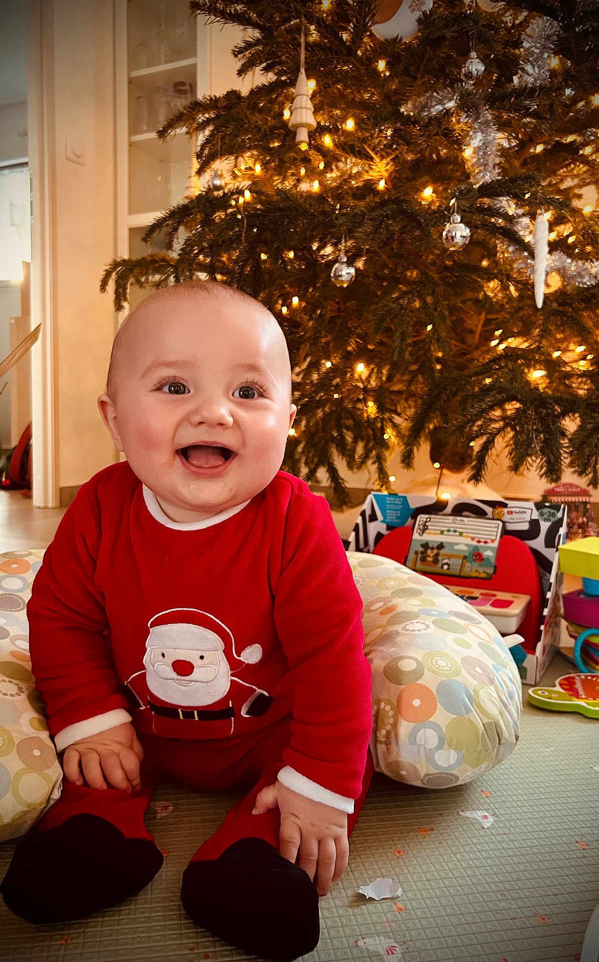 Léandre a rejoint le concours — aidez-le/la à gagner de superbes lots ! baby, child, smiling, christmas_tree, holiday, festive, indoors, red_clothing, toy, cushion, floor, decorations, lights, happy, sitting, cute, face, home, seasonal, celebration