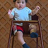 toddler, child, high_chair, wooden_furniture, curly_hair, grey_shirt, red_shorts, socks, indoor, lattice_wall, yellow_floor, baby, person, seated, cute, curious, young_child, portrait, casual_clothing, furniture