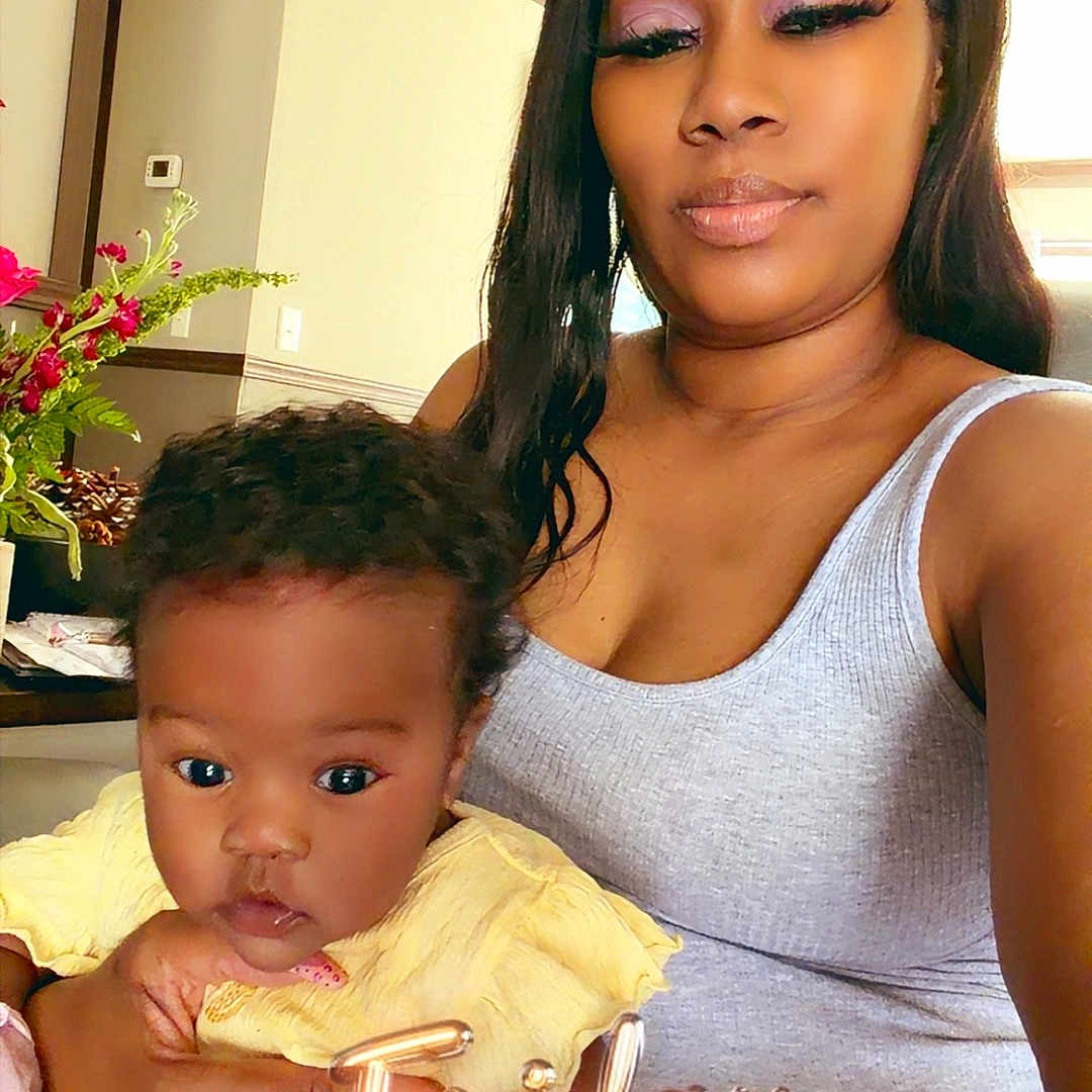 Demyah is registered to the contest to win money with this photo: baby, casual, cozy, curly_hair, face, family, furniture, holding, home, indoor, natural_light, person, plant, portrait, skin, smile, tank_top, text_overlay, woman, yellow_clothing